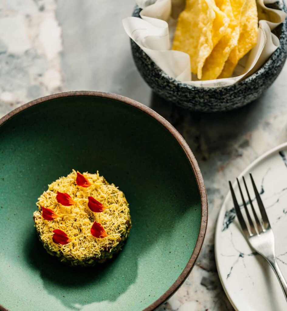 Savory dish topped with crispy shredded garnish and red petals, served with a side of chips.