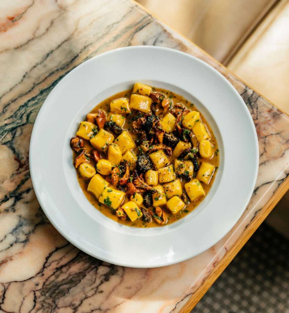 Gnocchi with mushrooms and herbs in a golden sauce, served in a white bowl.