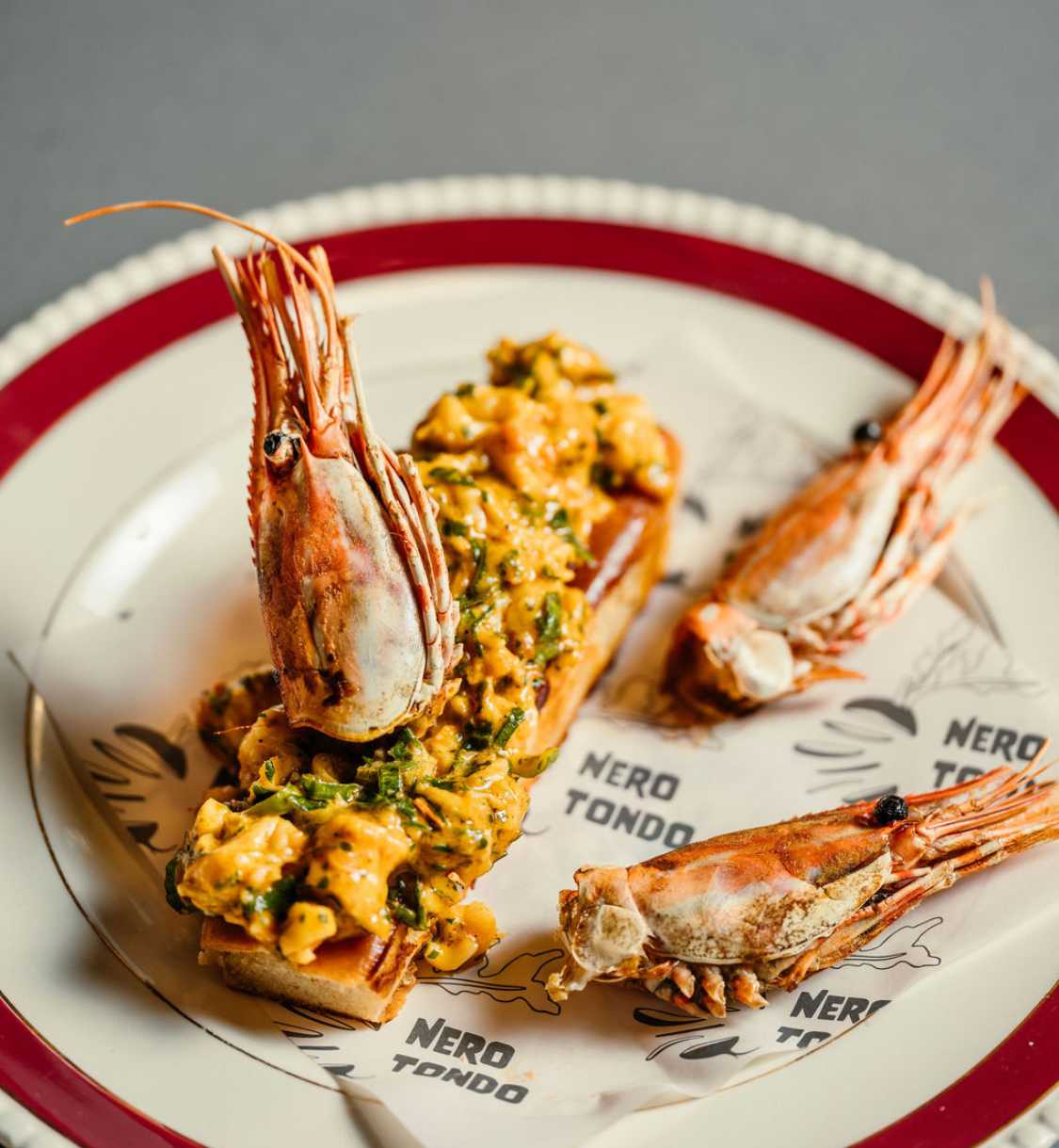 Toasted roll topped with prawn and seafood mixture, garnished with whole shrimp heads.