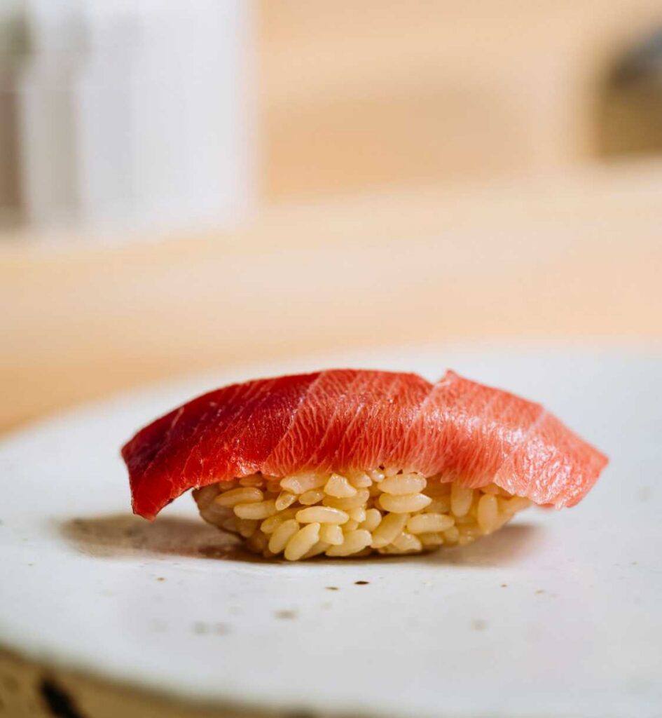 Close-up of sushi with fatty tuna atop vinegared rice on a white plate.