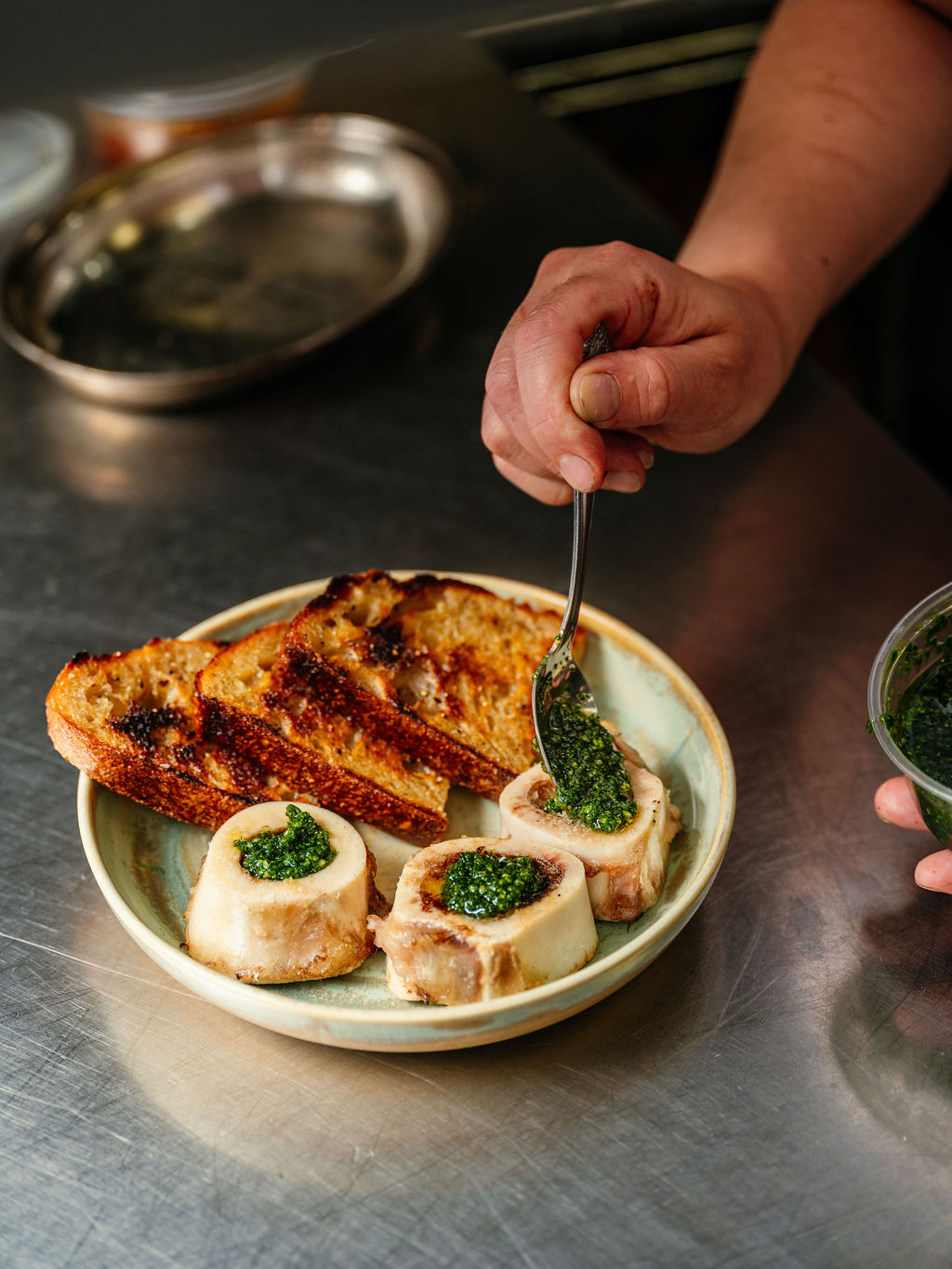 Un cuisinier nappe de sauce verte aux herbes trois os à moelle rôtis, servis avec du pain grillé, au passe.