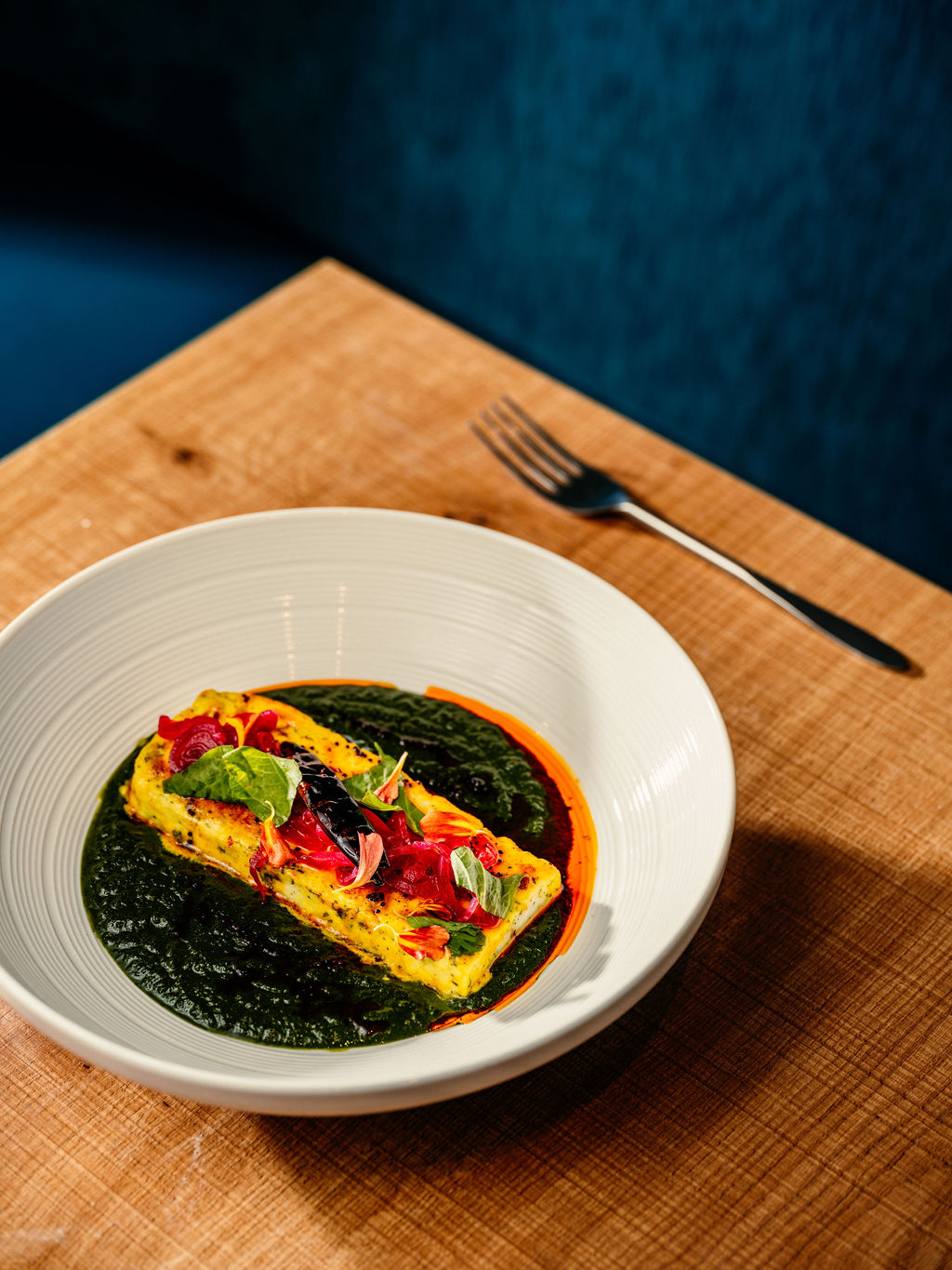 Bloc de paneer grillé et mariné sur une purée d'épinards foncée, garni de jeunes pousses et de fleurs, bol blanc.