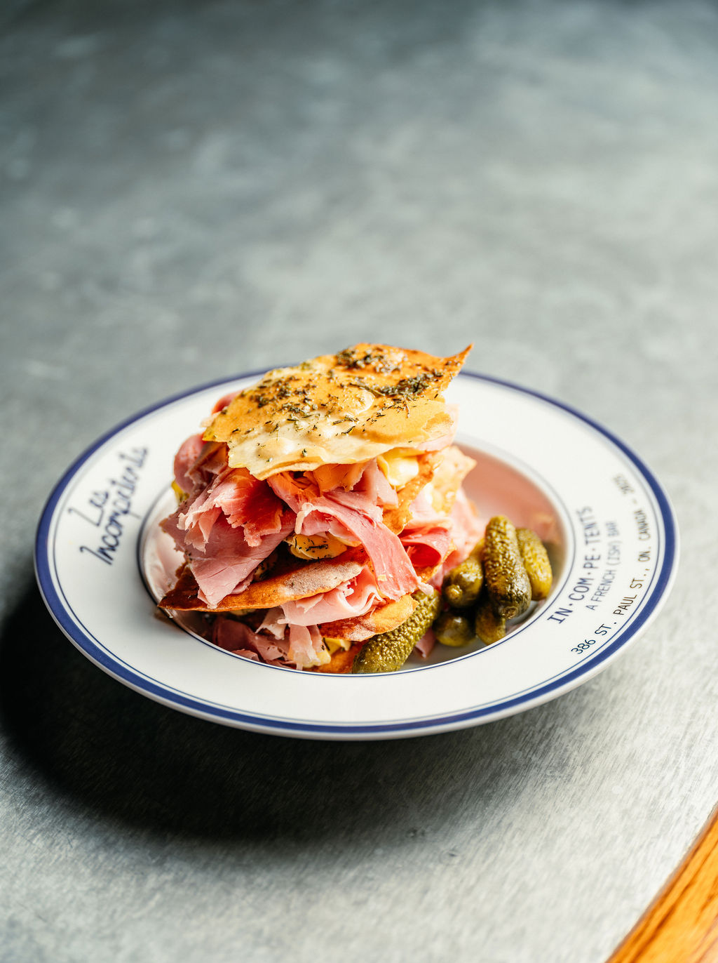 Tranches de jambon et tuiles de fromage avec cornichons, assiette bordée de bleu griffée Les Incompétents.