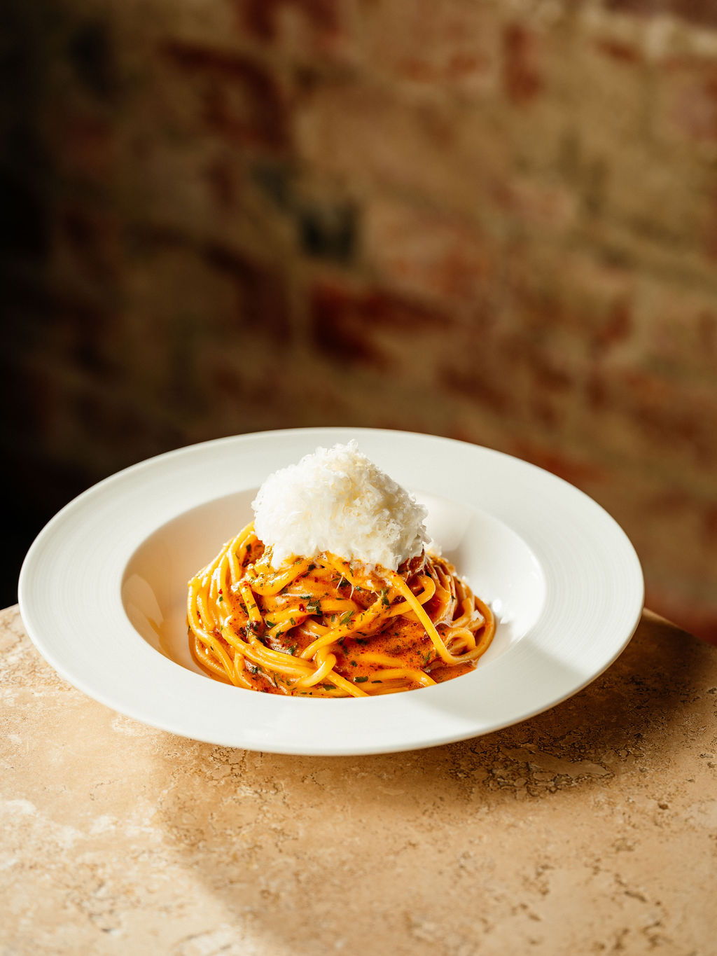 Spaghettis en sauce tomate au chili crisp, couronnés d'un monticule de fromage finement râpé, dans un bol blanc.