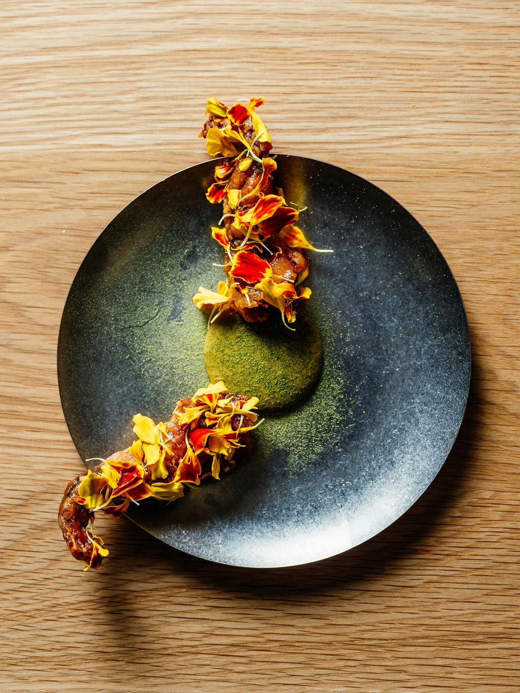 Bouchées glacées et pétales d'œillet d'Inde en arc sur une assiette sombre, près d'une purée verte, sur chêne.