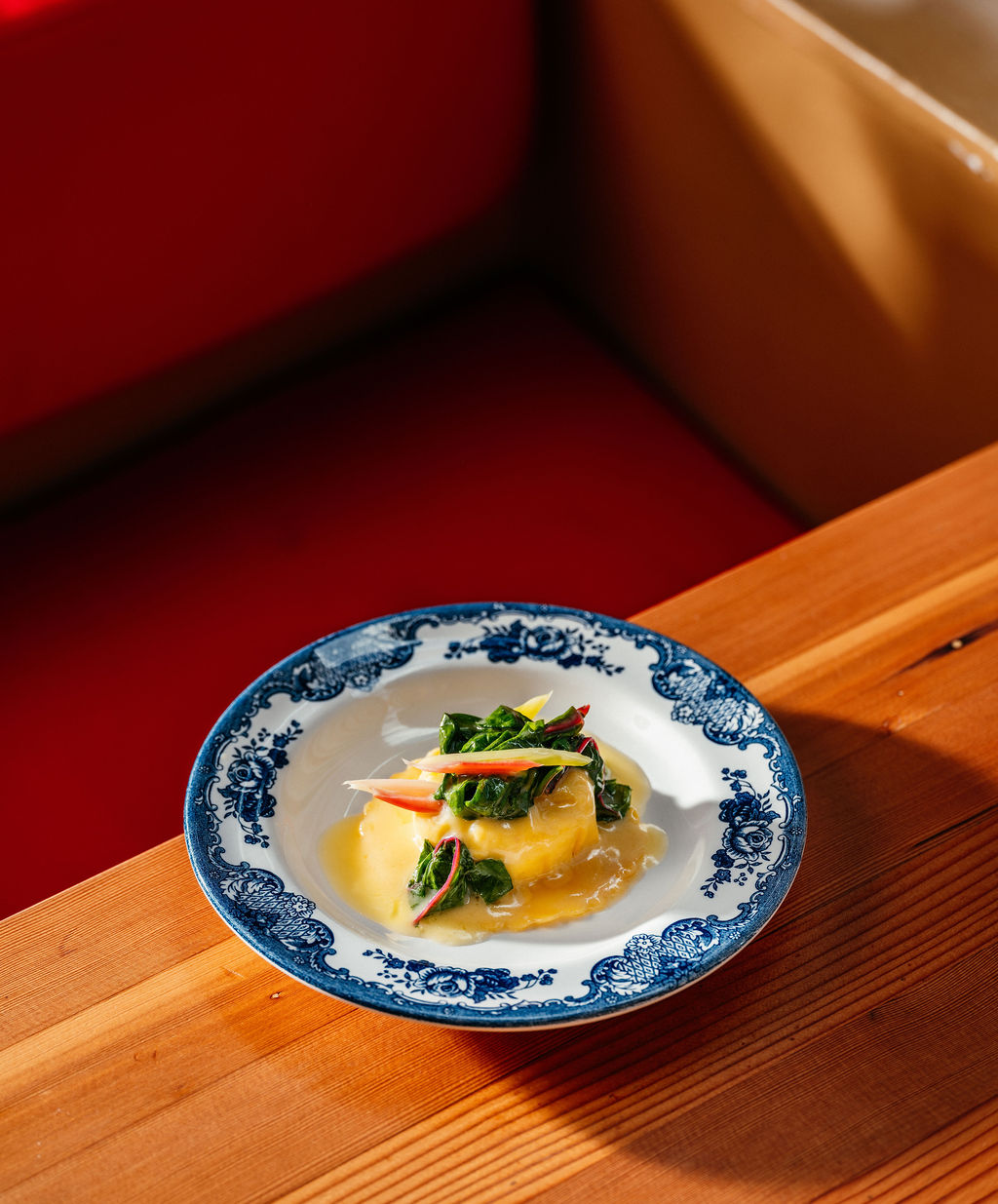 Pâte farcie en sauce au beurre avec bettes à carde, dans une assiette fleurie bleue baignée de soleil.