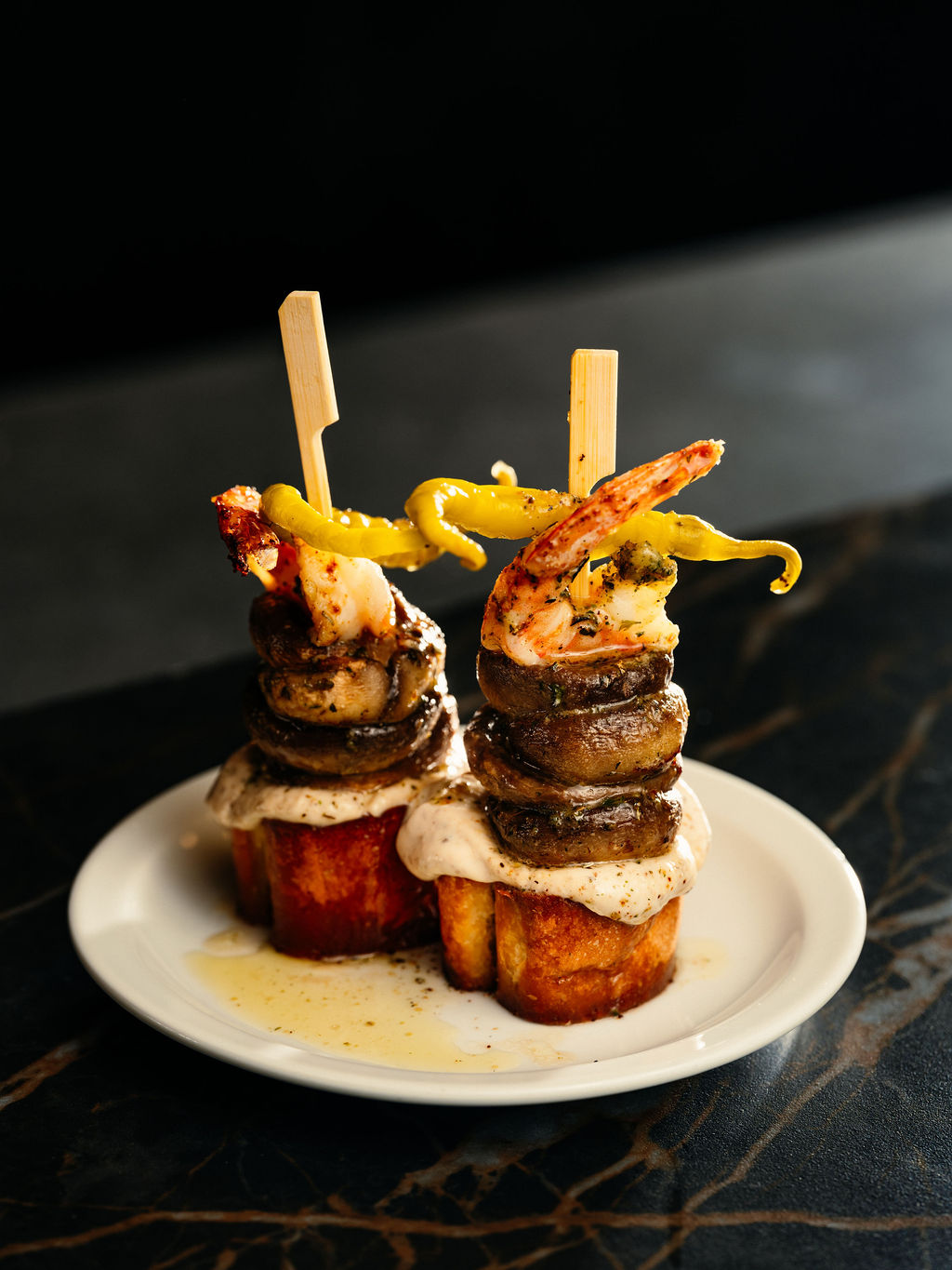 Deux pintxos en brochette: crevette, champignons et piments marinés sur pain grillé, avec sauce crémeuse.